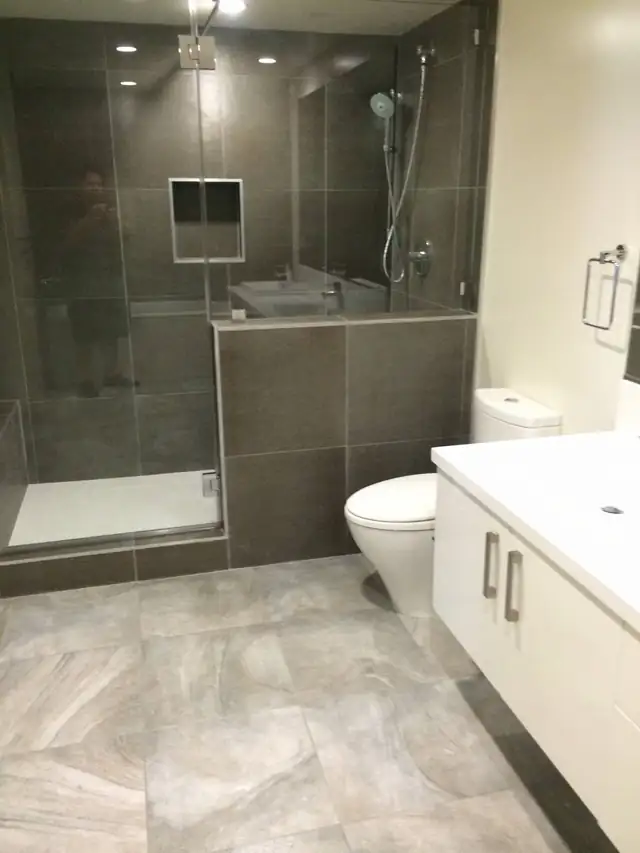 Walk-in shower with dark gray wall tile, a frameless glass panel, a recessed niche and large-format floor tile