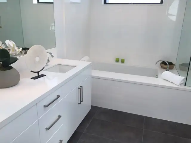 Wixom, MI bathroom remodel with a white modern vanity and quartz top, deep soaking tub with white tile surround and dark floor tile