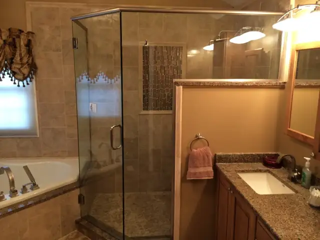 Novi, MI bathroom with a neo-angle frameless glass shower enclosure, beige tile walls with a decorative stripe and a corner jetted tub