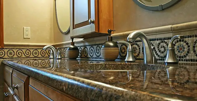 Bathroom vanity with a granite countertop, brushed nickel faucets and a decorative mosaic tile border