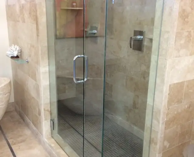 Travertine tile shower with a frameless glass door, corner shelf and mosaic floor