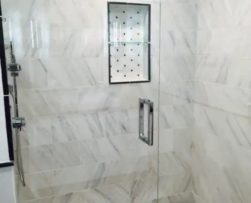Walk-in shower with white marble-look tile, a mosaic niche and a frameless glass door with chrome handle