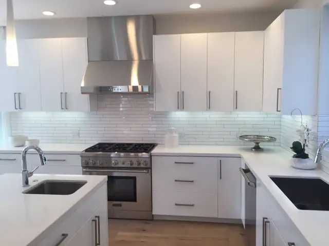 Modern white kitchen with flat-panel cabinets, white quartz counters, glass tile backsplash and a stainless range hood