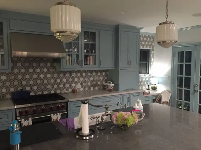 Kitchen with blue-gray cabinets, hexagon tile backsplash, glass-front uppers and two drum pendant lights