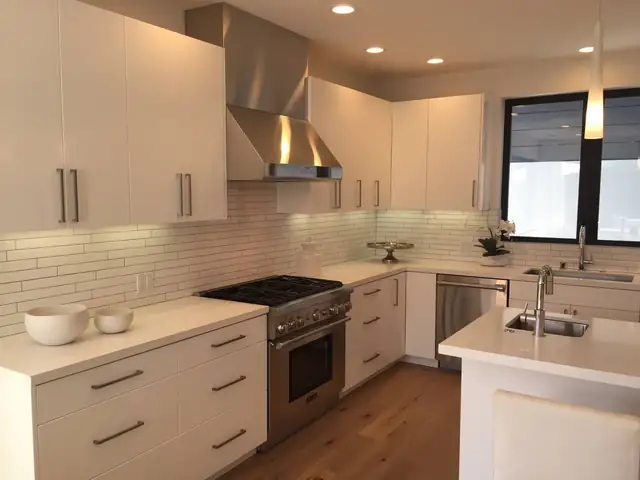 Modern white kitchen with flat-panel cabinets, a stainless range hood, white linear tile backsplash and oak floors